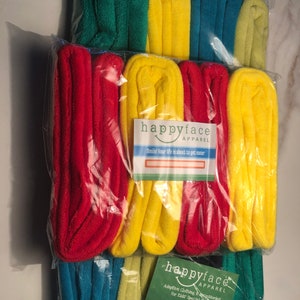 May include: A package of 12 colorful, rolled-up towels. The towels are in various colors, including red, yellow, green, and blue. The package is labeled "happyface APPAREL" and says "Adaptive Clothing & Accessories for Kids Special Needs. Sizes 2-15."