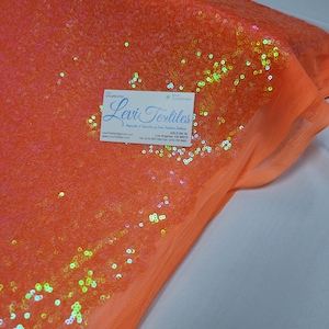 Peut inclure: Des paillettes orange irisées sur un tissu transparent. Le tissu est plié et les paillettes sont visibles des deux côtés. Le tissu est de couleur orange clair et les paillettes sont de différentes couleurs, notamment le vert, le bleu et le violet.