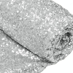 Puede incluir: Tela de lentejuelas plateadas, un primer plano del material brillante. Las lentejuelas son pequeñas y están muy juntas, creando un efecto brillante.