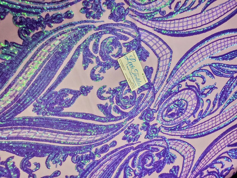 May include: Purple iridescent sequins on a pink fabric with a damask pattern. The fabric is for sale and the business card for "Levi Textiles" is visible in the image.