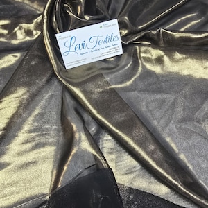 May include: Metallic fabric in shades of gold and bronze, with a shimmering, reflective quality. The fabric is draped, creating folds and shadows. A business card with the text "Levi Textiles" is visible.