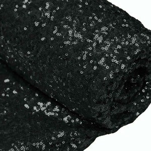 Könnte beinhalten: Schwarzer Paillettenstoff mit glänzender Oberfläche. Der Stoff ist aufgerollt und die Pailletten sind sichtbar.