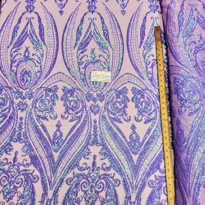 May include: Purple iridescent sequins on a pink mesh fabric with a damask pattern. The fabric is measured with a ruler in inches.