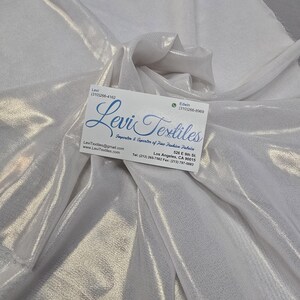 May include: White, shimmering fabric with soft folds. A business card with the text "Levi Textiles" is placed on the fabric. The fabric appears to be a lightweight material, possibly for fashion or design.