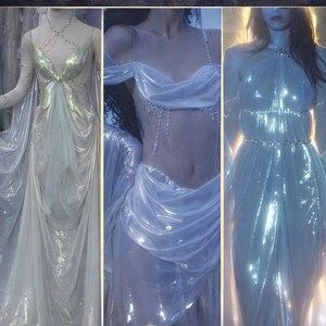 May include: Image features three elegant gowns in shimmering, flowing fabrics. The gowns are in shades of white and silver, with intricate detailing. Text at the top reads "GORGEOUS GOWNS DESIGNED WITH OUR FABRIC". The bottom text says "Firefly Path's Stunning Creations!"