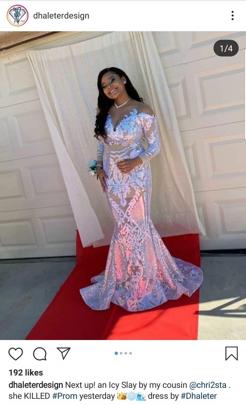 May include: A woman wearing a white sequined gown with a plunging neckline and long sleeves. The gown has a mermaid silhouette and is adorned with floral embroidery. The woman is standing on a red carpet.