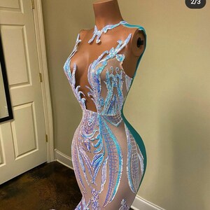 May include: A mermaid-style gown with a sheer bodice and a teal skirt. The bodice is covered in iridescent sequins and features a floral design. The skirt is made of a smooth fabric and flows to the floor.