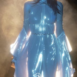 May include: A shimmering, light blue gown with a halter neckline and flowing sleeves. The dress features a silver chain belt and delicate chain accents on the arms. The image is set against a soft, glowing background, with the text "FIREFLY PATH" at the bottom.