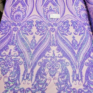 May include: Purple iridescent sequins on a light pink fabric with a damask pattern. The fabric is measured with a ruler in inches.