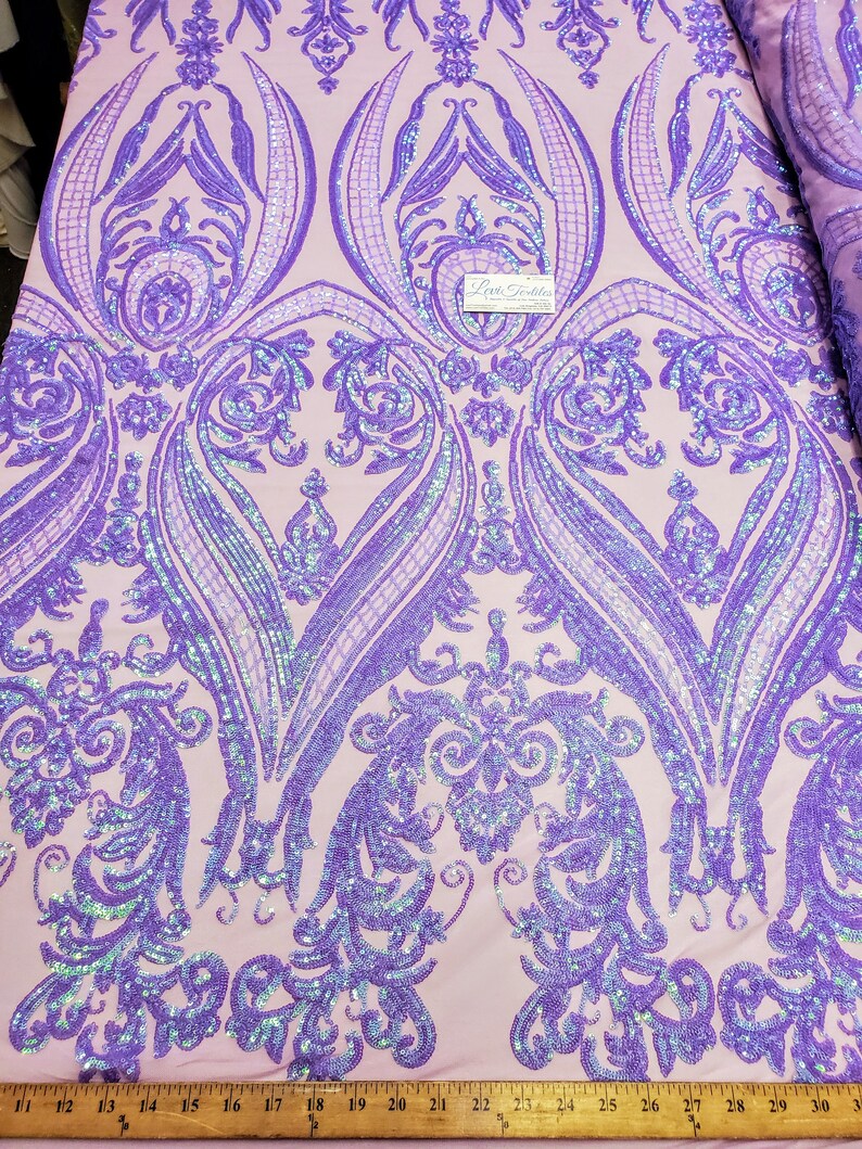 May include: Purple iridescent sequins on a light pink fabric with a damask pattern. The fabric is measured with a ruler in inches.