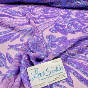 May include: Purple iridescent sequin fabric with a floral pattern. The fabric is sheer and has a mesh backing. The fabric is folded in half and a business card for Levi Textiles is visible in the bottom right corner.