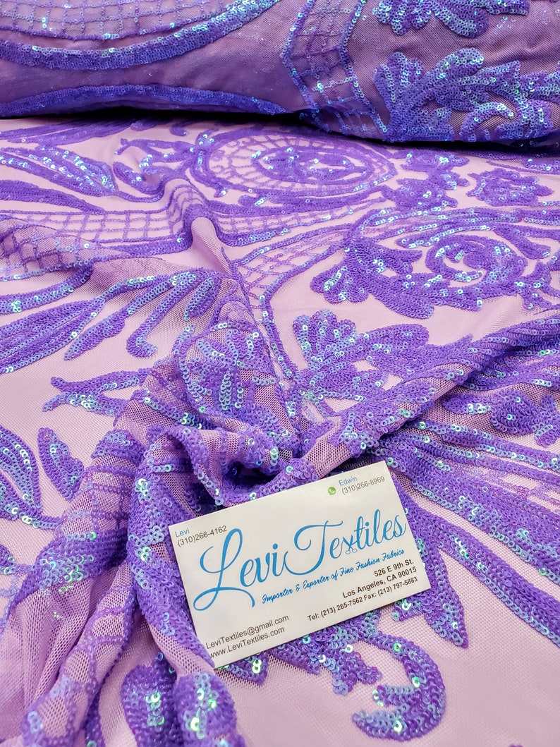 May include: Purple iridescent sequin fabric with a floral pattern. The fabric is sheer and has a mesh backing. The fabric is folded in half and a business card for Levi Textiles is visible in the bottom right corner.