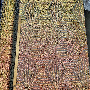 May include: A close-up of iridescent gold and black geometric patterned fabric with sequins. The fabric is measured with a ruler in inches.