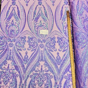 May include: Purple iridescent sequins on a light pink mesh fabric with a damask pattern. The fabric is measured with a ruler in inches.