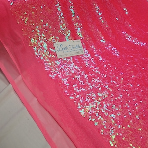 May include: Pink iridescent sequins on a sheer pink fabric. The fabric is folded in half and the sequins are visible on both sides. The fabric is a lightweight material and would be ideal for a dress or skirt. The fabric is also available in other colors.