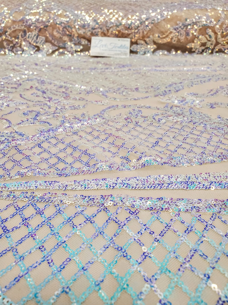 May include: Close-up of iridescent blue, purple, and white sequins sewn onto a beige mesh fabric. The sequins are arranged in a diamond pattern.