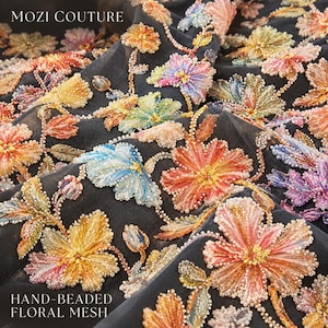 May include: Black mesh fabric featuring intricate hand-beaded floral embroidery in vibrant shades of pink, orange, yellow, blue, and purple. The text MOZI COUTURE and HAND-BEADED FLORAL MESH is printed in white on the fabric surface.