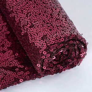 May include: A roll of burgundy sequin fabric. The sequins are small and round, and the fabric has a mesh backing.