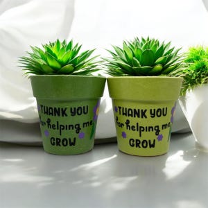 May include: Two small green plant pots, each with a succulent plant. The pots are inscribed with "THANK YOU for helping me GROW" in black, with purple flower accents. One pot is a darker shade of green than the other.