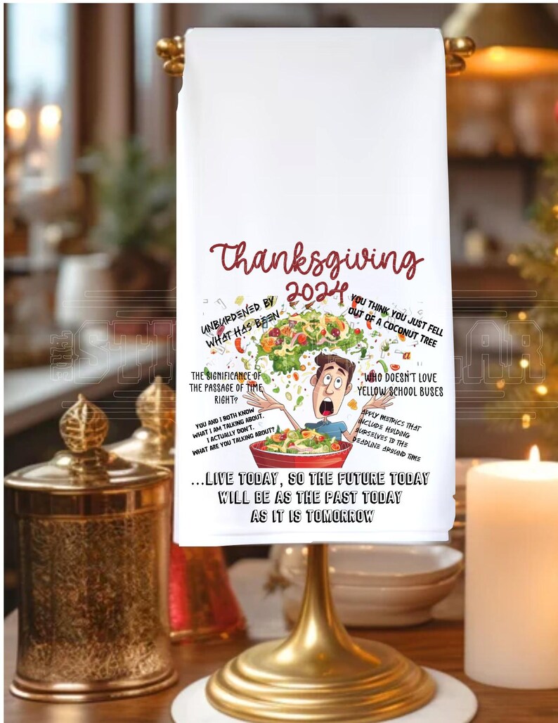 May include: White kitchen towel with a Thanksgiving 2024 design. The design features a cartoon man with a salad bowl on his head, surrounded by food and text. The text includes "Unburdened by what has been", "The significance of the passage of time right?", "You think you just fell out of a coconut tree", "Who doesn't love yellow school buses", "Apply metrics that include holding deadlines around time", and "...Live today, so the future today will be as the past today as it is tomorrow."