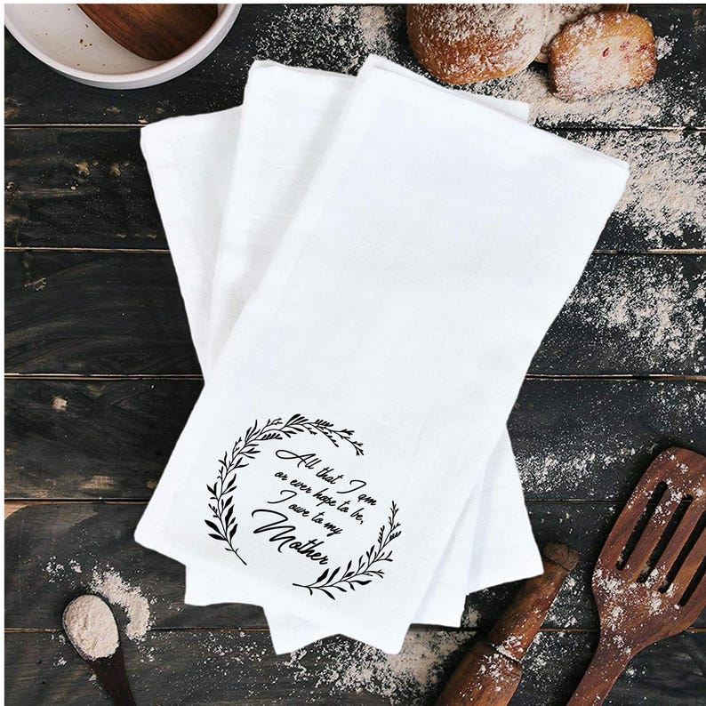 May include: White kitchen towels with a black floral wreath and the text "All that I am or ever hope to be, I owe to my Mother".