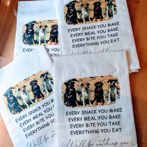 May include: Four dogs are sitting in a row on a white kitchen towel. The towel has the text "Every snack you make, every meal you bake, every bite you take, everything you eat. We'll be watching you." printed on it.