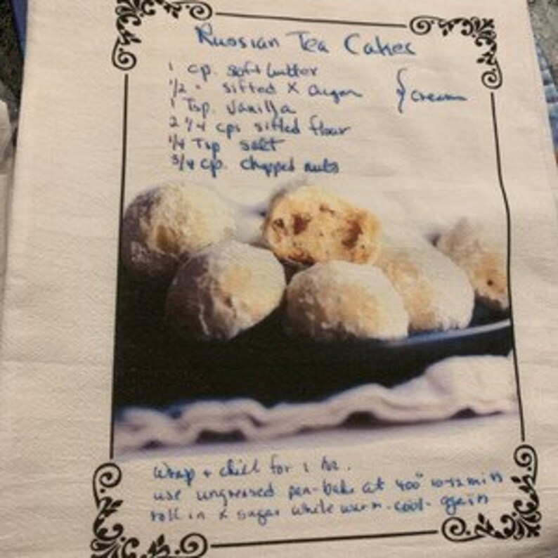 May include: A handwritten recipe for Russian Tea Cakes with a photo of the finished product. The recipe calls for 1 cup of soft butter, 1/2 cup of sifted powdered sugar, 1 teaspoon of vanilla extract, 2 1/4 cups of sifted flour, 1/4 teaspoon of salt, and 3/4 cup of chopped nuts.