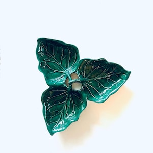 Może przedstawiać: Błyszczący, szmaragdowozielony ceramiczny talerz w kształcie liścia. Talerz składa się z trzech połączonych liści, każdy ze szczegółowym unerwieniem. Projekt to dekoracyjny element akcentujący, odpowiedni do serwowania lub ekspozycji.