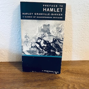 Pode incluir: Um livro vintage intitulado "Preface to Hamlet" de Harley Granville-Barker. A capa é azul escuro com texto branco e uma ilustração a preto e branco de uma cena da peça. Um clássico da crítica shakespeariana.
