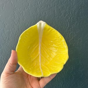 May include: A yellow ceramic bowl shaped like a lettuce leaf. The bowl has a white center and is perfect for serving snacks or dips.