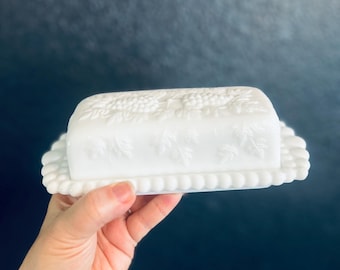 ウェストモアランド製ミルクガラス製バター皿、ブドウとブドウの葉の模様が浮き彫りにされ、縁は波型にカットされている。