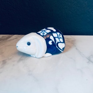 May include: A ceramic rabbit figurine, primarily white with blue floral patterns on its back. The rabbit has blue eyes and a detailed design. The figurine is a decorative item, likely for home decor or a collector's piece.