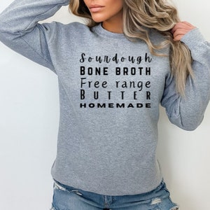 May include: A heather gray sweatshirt with the words "Sourdough, Bone Broth, Free range, BUTTER, HOMEMADE" printed in black. The sweatshirt is a crew neck style and has long sleeves.