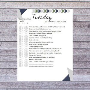 May include: A white cleaning checklist titled "Tuesday Cleaning Checklist" with a wooden background. The checklist includes tasks like cleaning the tub, sinks, toilet, and other bathroom surfaces. Decorative geometric shapes in blue, green, and gray are at the top and bottom.