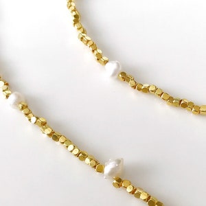 May include: A gold chain necklace with small, square-shaped beads and white pearls. The necklace is delicate and feminine.