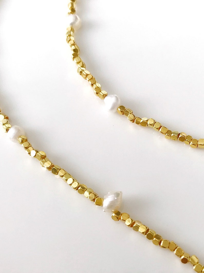 May include: A gold chain necklace with small, square-shaped beads and white pearls. The necklace is delicate and feminine.