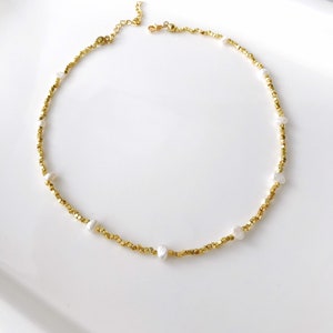 May include: A gold necklace with small gold beads and white pearl accents.