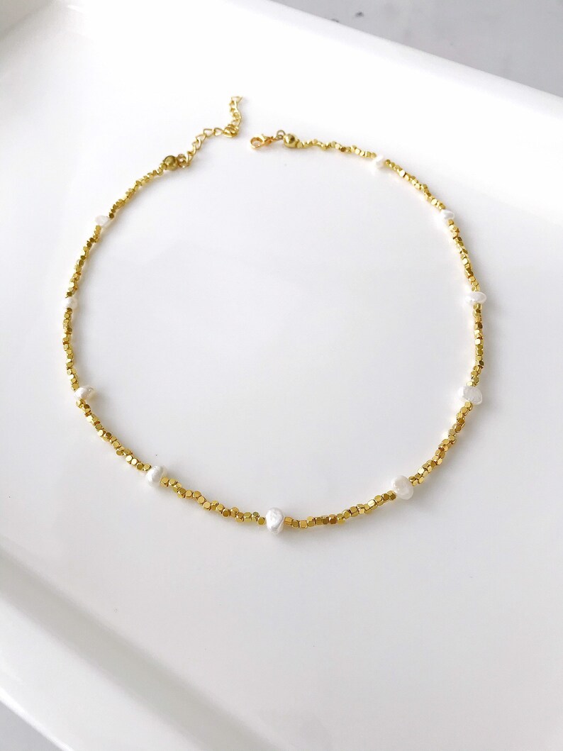 May include: A gold necklace with small gold beads and white pearl accents.