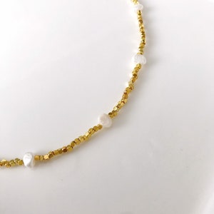 May include: A gold necklace with small gold beads and white pearl accents.