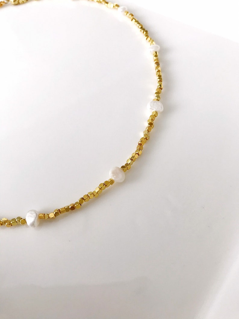 May include: A gold necklace with small gold beads and white pearl accents.