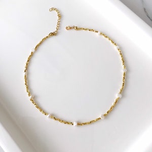 May include: A gold necklace with small gold beads and white pearl accents.