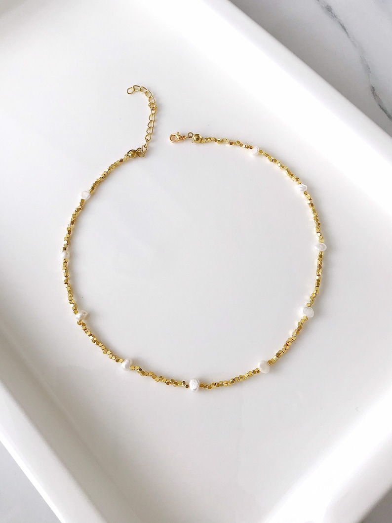 May include: A gold necklace with small gold beads and white pearl accents.