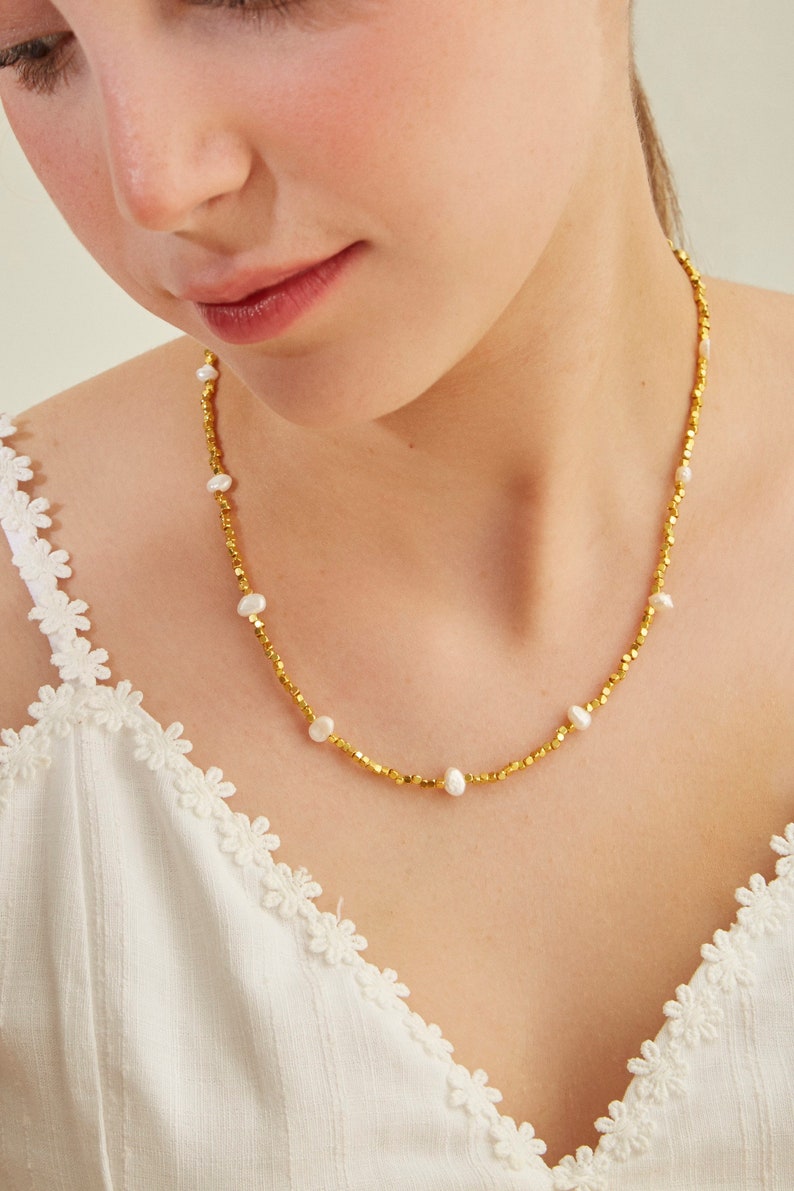 May include: A gold necklace with small, round beads and white pearls. The necklace is delicate and feminine.