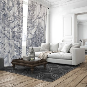 Könnte beinhalten: Ein weißes Sofa mit Kissen steht in einem Wohnzimmer mit einem gemusterten Vorhang, einem Holz-Couchtisch und einem Teppich mit kreisförmigem Muster. Eine Tür führt in ein anderes Zimmer mit einem Bett.
