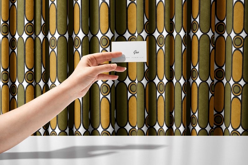May include: A white business card with the text "Gina" and "www.ginafranklin.com" printed on it. The card is being held in front of a green and gold patterned curtain.
