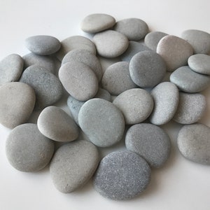 May include: A pile of smooth, gray and white stones. The stones are various sizes and shapes, and they are arranged in a random pattern.