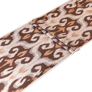 May include: A brown and cream patterned fabric with an ikat design. The fabric is folded in half and has a white background.