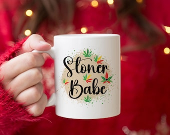 May include: White ceramic mug with a green, red, and yellow marijuana leaf design and the text "Stoner Babe" in black cursive lettering.