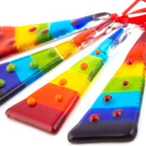 Op de afbeelding: Vijf regenboogkleurige glazen ornamenten met rode stippen. Elk ornament heeft de vorm van een traan en heeft een andere kleur van de regenboog.
