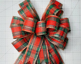 May include: A red and green plaid bow with gold trim. The bow is made of ribbon and is tied in a knot. The bow is a festive decoration for the holidays.